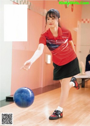 A young woman holding a red bowling ball in a bowling alley.
