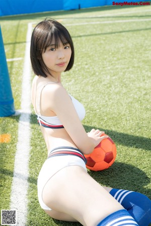 A woman in a bikini sitting on a soccer field with a soccer ball.