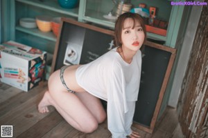 A woman in a white shirt and black and white thong standing in a kitchen.