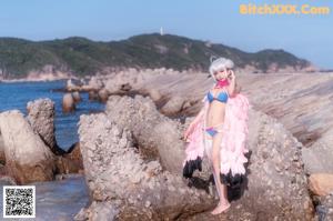 A woman in a bikini sitting on a rock by the ocean.