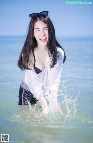 A woman in a black bikini and sunglasses on the beach.
