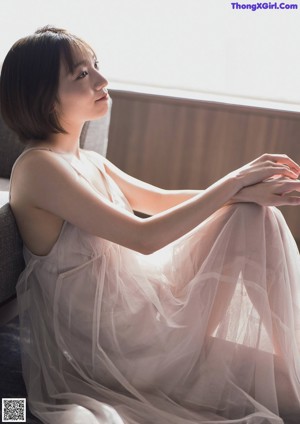 A woman in a white robe sitting by a window.