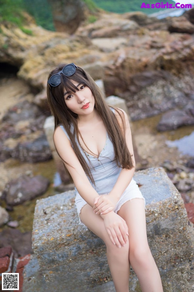 A woman sitting on a rock by the water.
