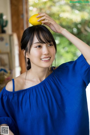 A woman sitting on a stool holding two lemons.