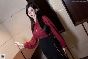 A woman in a red shirt and black skirt sitting on a table.