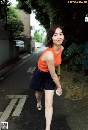 A woman in an orange top and black shorts posing for a picture.