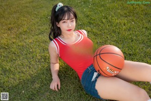 A woman in a red shirt and denim shorts holding a basketball.