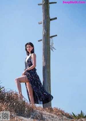 A woman in a white dress standing in front of a hedge.
