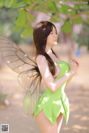A woman in a green dress posing next to a tree.