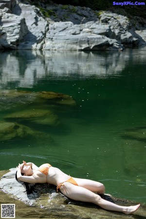 A woman in a bikini standing on a rock by a river.