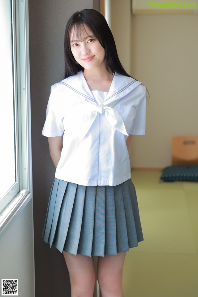 A woman in a school uniform standing by a window.