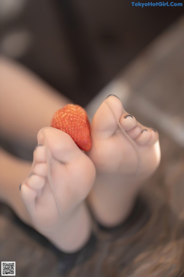 A person holding a strawberry in their bare feet.